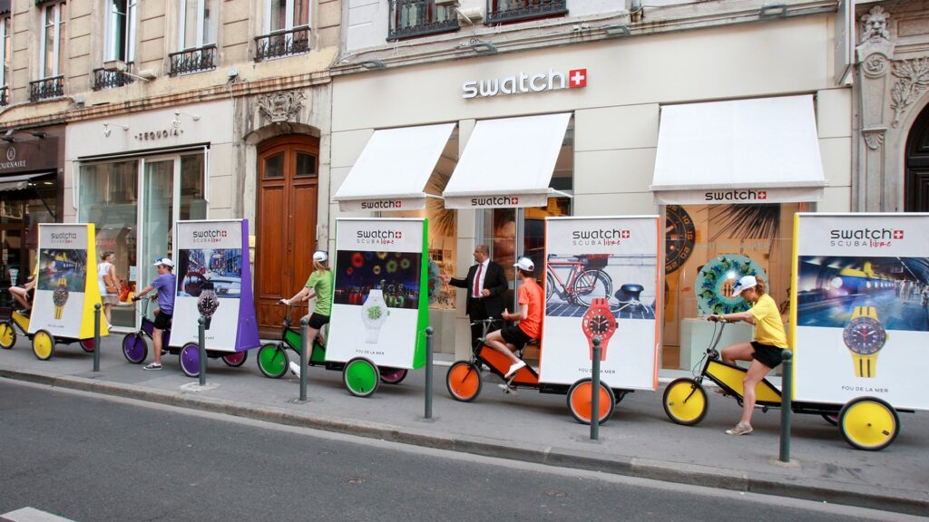 swatch-horlogerie-campagne-velo-publicitaire-avec-hotes-affichage-mobile-tapage-medias-min